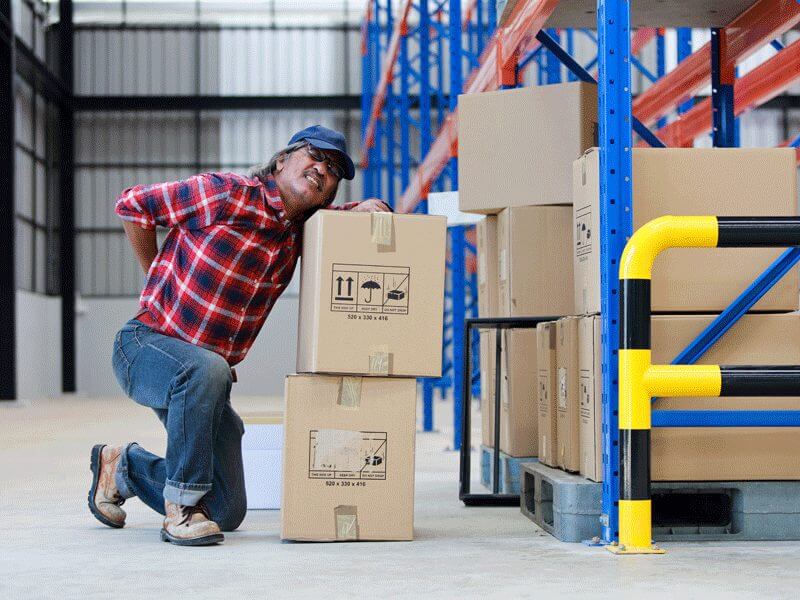A man experiencing backpain at work trying to lift boxes