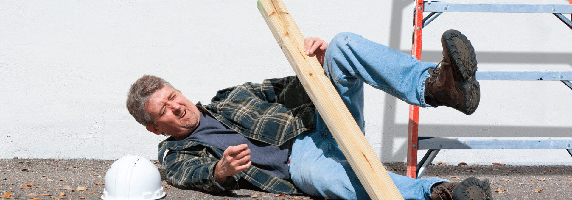 A man with a two by four who has fallen over at a construction site